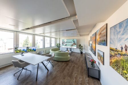 moderner, lichtdurchfluteter Büroraum mit Beratungstisch, Sofa und farbenprächtigen Bildern an der Wand